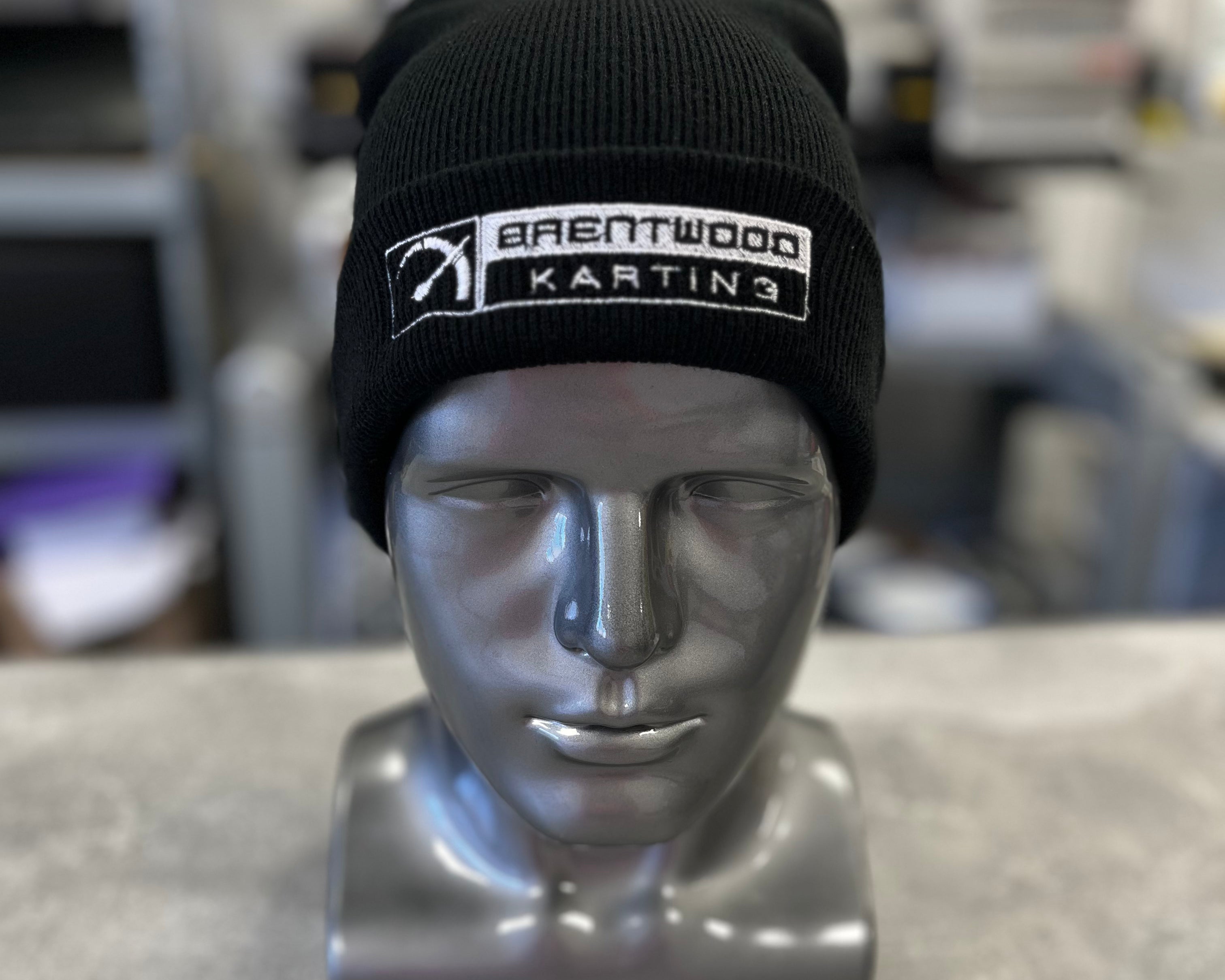 Black knitted beanie hat embroidered with the Brentwood Karting logo, showcased on a silver mannequin head, part of the official branded merchandise collection.