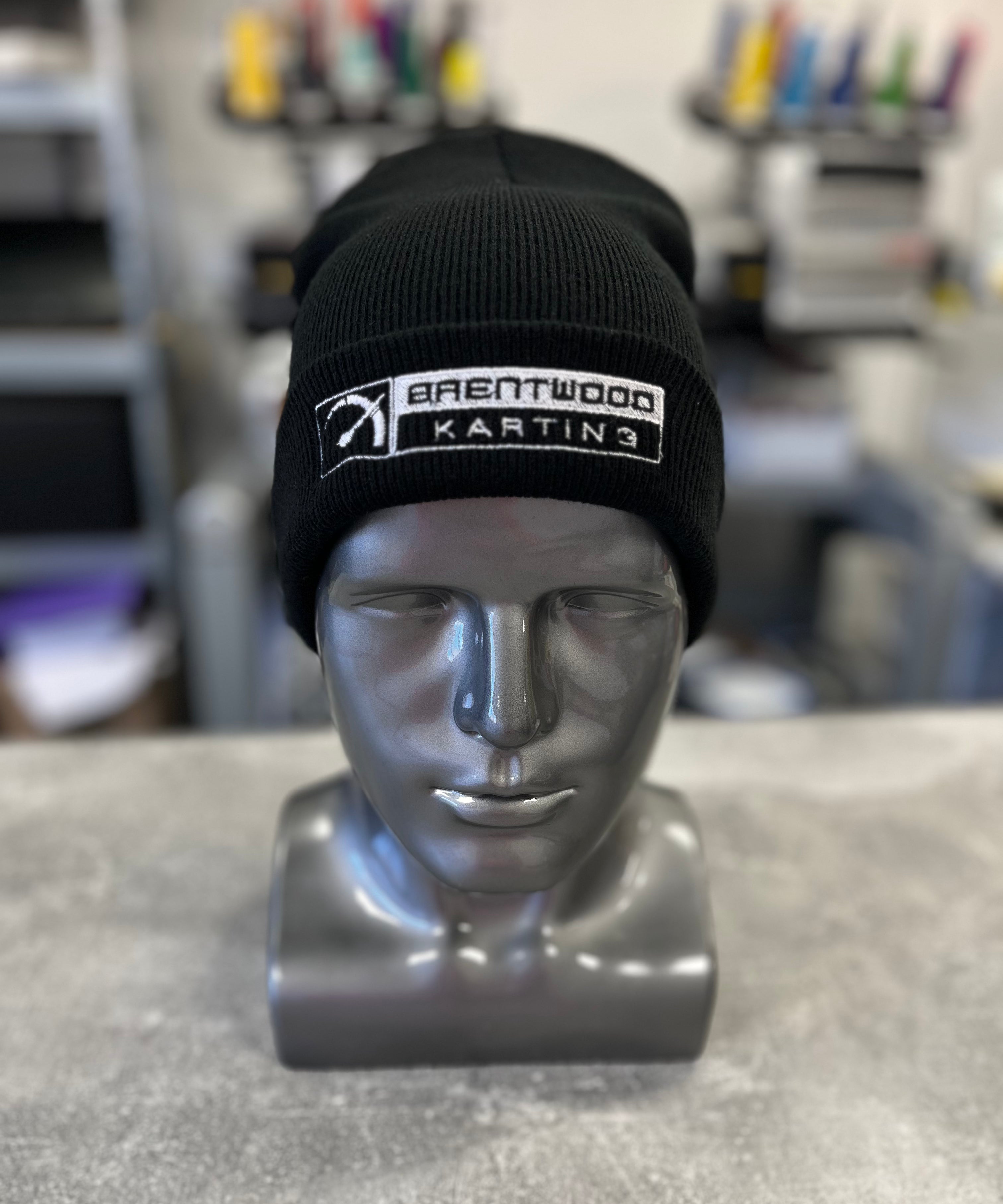 Black knitted beanie hat embroidered with the Brentwood Karting logo, showcased on a silver mannequin head, part of the official branded merchandise collection.