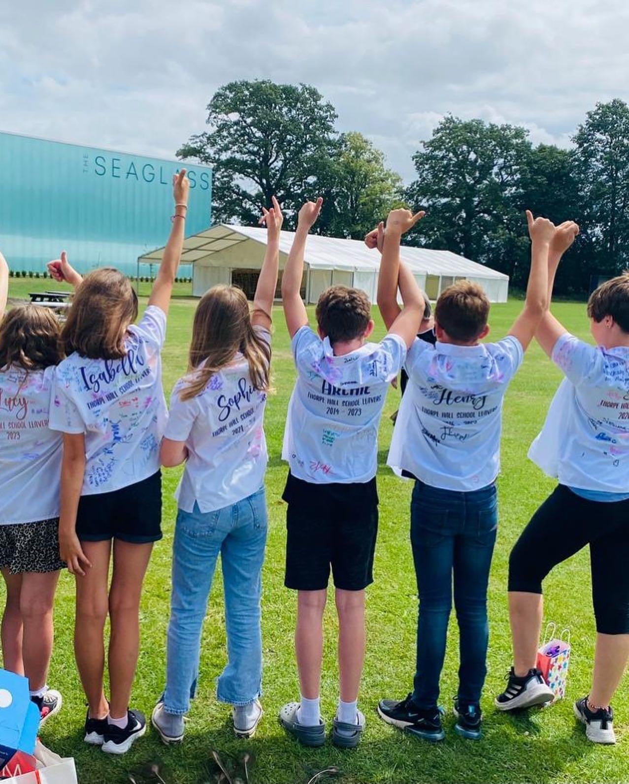 Group of children wearing personalised Thorpe Hall School leavers shirts, standing together on a playing field.
