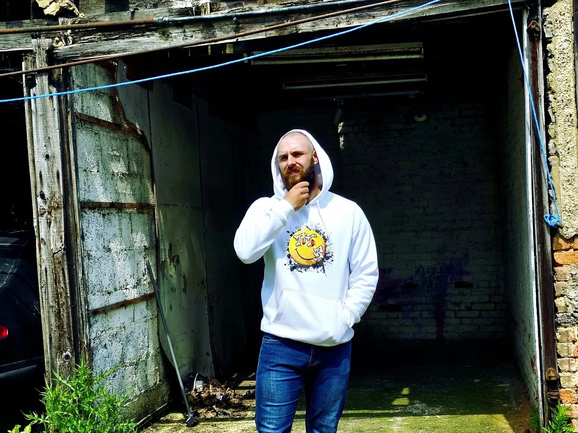 Promotional image for To The Bone showcasing a model in a white hoodie with a graffiti-inspired smiley face design, styled in a raw industrial backdrop to highlight the brand’s edgy streetwear aesthetic.